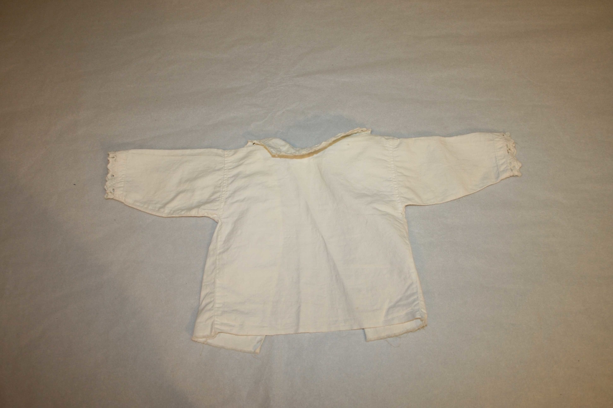 Langerma barneskjorte av kvitt bomullsstoff, med blondekrage og band til å knyte bak.