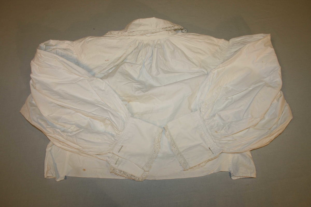 Kvit bomullsskjorte i tradisjonell form. Lange ermar, blonder på krage og mansjettar. Noko flekkut.
