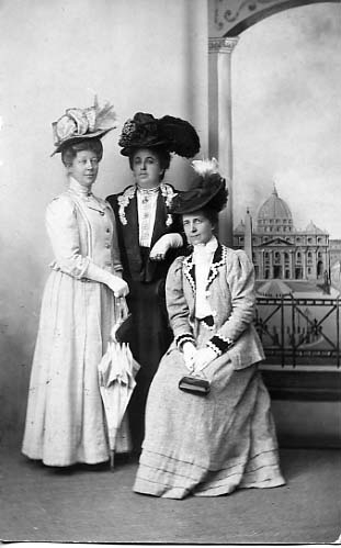 Tre eleganta kvinnor med parasoll och hatt i en ateljé.