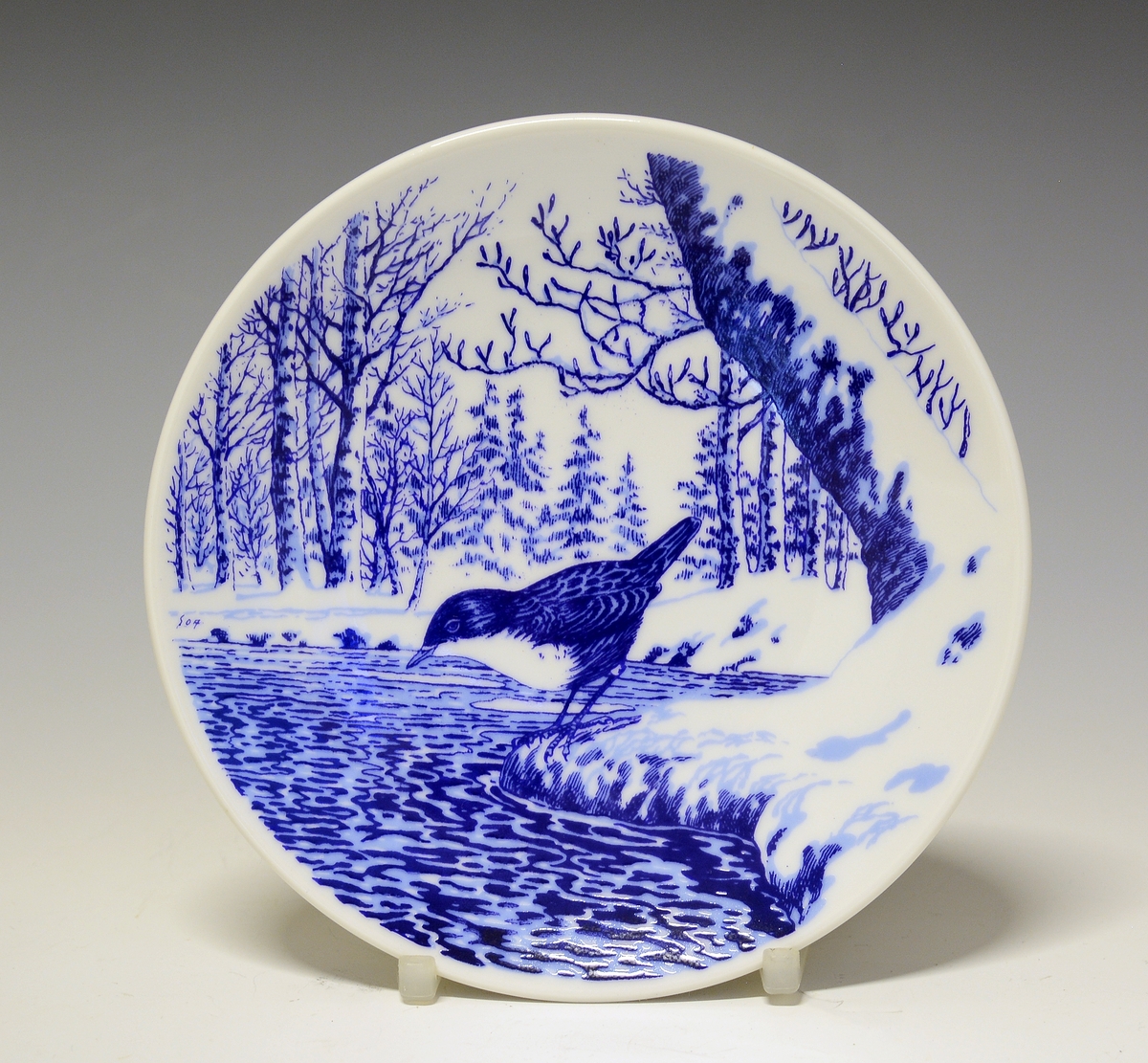Platte i porselen med blå trykkdekor. Fossekall ved vann i vinterlandskap.