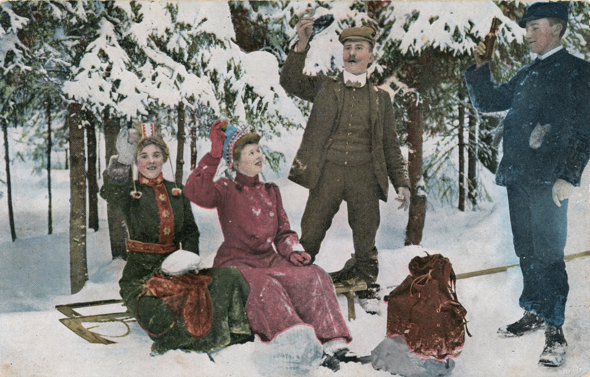 Postkort. Det håndkolorerte fotografiet på kortets fremside viser menn og kvinner på aketur i vinterlandskap.