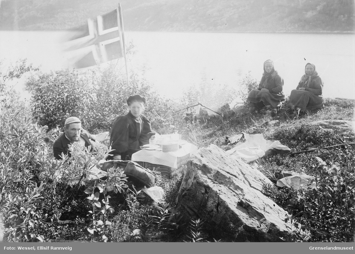 Rast ved Langfjorden på tur til Vaggetem, juli 1897. Mannen som ligger er Cand. Jur. Hillestad og kvinnen er frk. Hagemann. De to samiske jentene til høyre i bildet er ukjente.