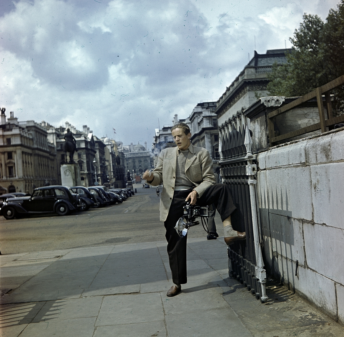 Fotografen Hans Malmberg med kameran i ena handen och en cigarett i den andra. Stadsmiljö.