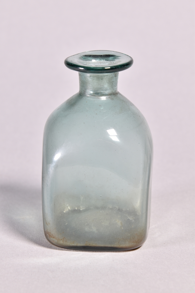 Flaska av grönt glas, kvadratisk med kort hals och utvikt mynning.