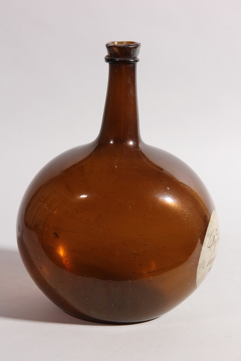 Flaska av brunt glas, rund med tillplattade sidor och hög hals.