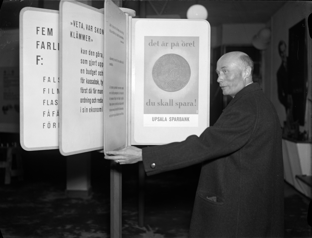 Bankdirektör J H Jönsson vid ett av text- och bildmontagen i Upsala Sparbanks propagandautställning "Spar för att köpa", Svartbäcksgatan 25