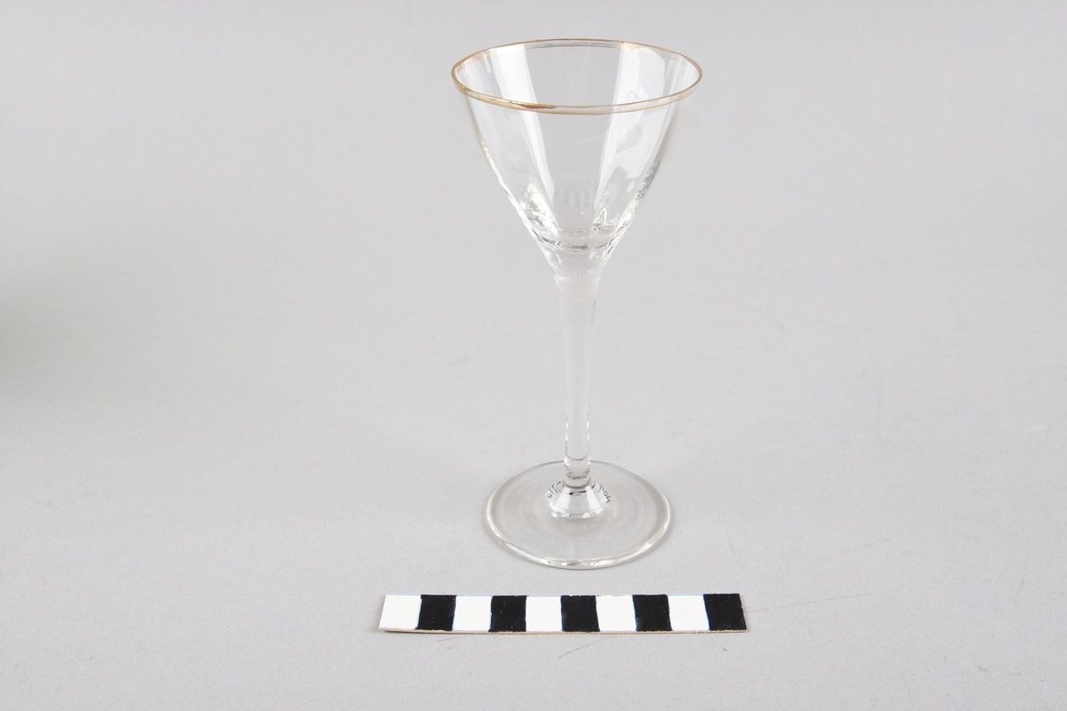 Drammeglas med konisk utforma korpus. Tynn, høg stett og rund fot. Korpus har ti vertikale liner. Drikkekanten er forgylla.