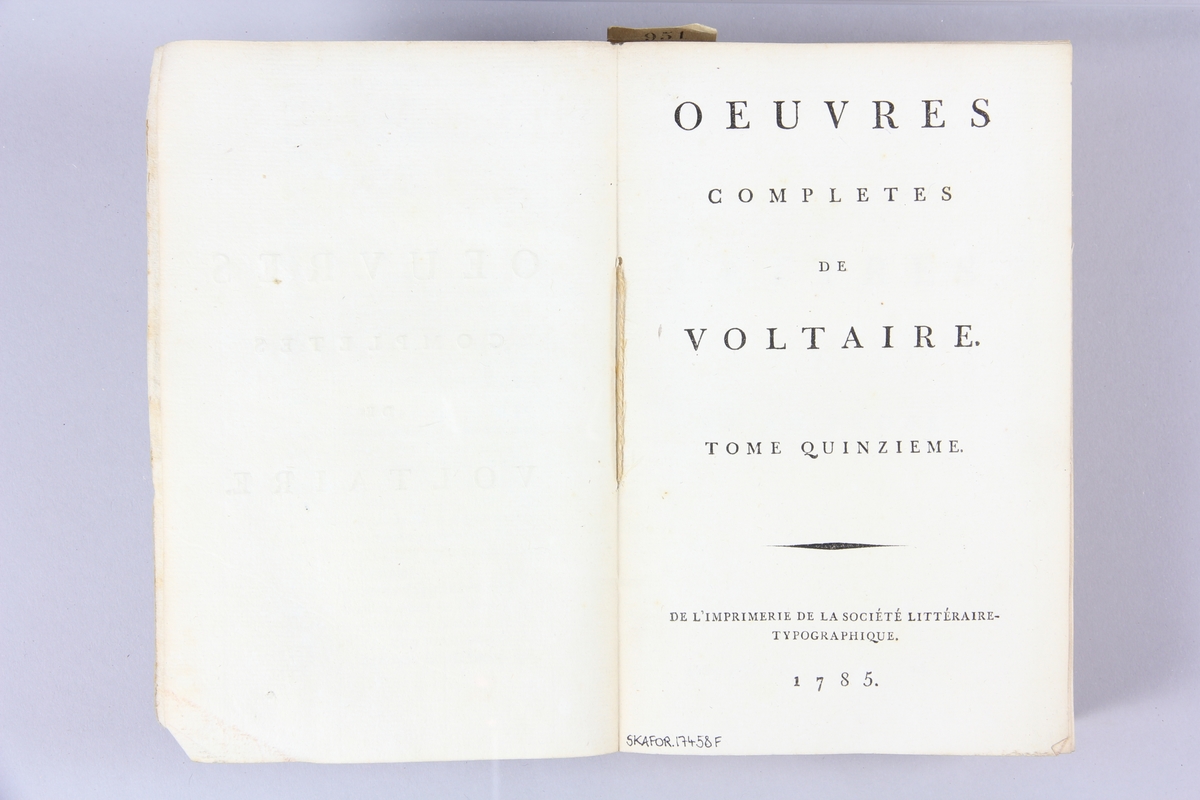 Bok, häftad,"Oeuvres complètes de Voltaire", del 15, tryckt 1785.
Pärm av gråblått papper, på pärmens baksida klistrad sida ur annan bok. Med skurna snitt. På ryggen klistrad pappersetikett med tryckt text samt volymens nummer. Ryggen blekt.