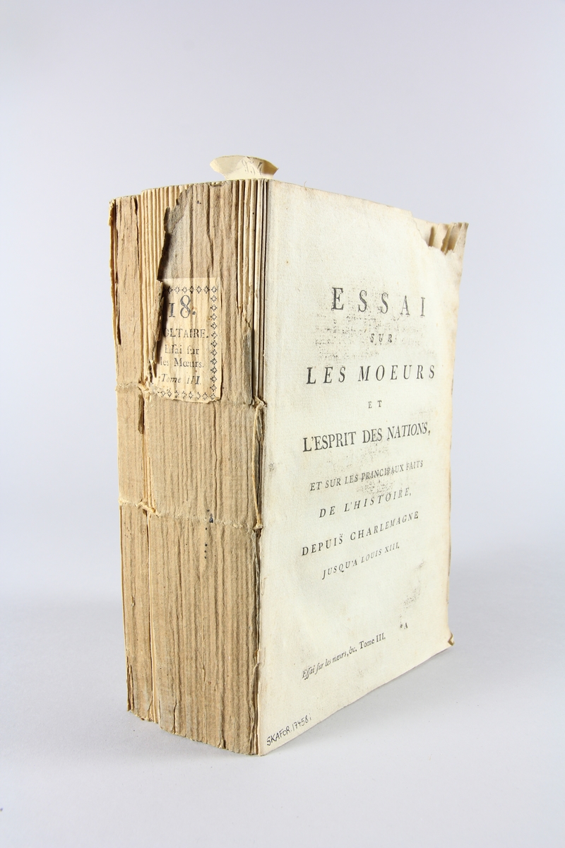 Bok, häftad,"Oeuvres complètes de Voltaire", del 18, tryckt 1785.
Pärm av gråblått papper, på pärmens baksida klistrad sida ur annan bok. Med skurna snitt. På ryggen klistrad pappersetikett med tryckt text samt volymens nummer. Ryggen blekt.