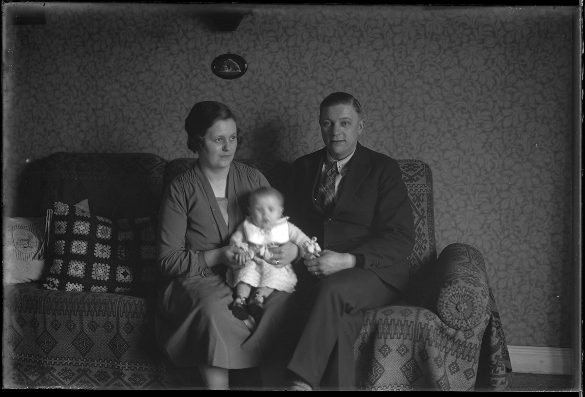 Familjen Pettersson sitter i en soffa. Sonen sitter i sin mammas knä och håller föräldrarna i handen. I fotografens egna anteckningar står det "Sven Pettersson med familj".