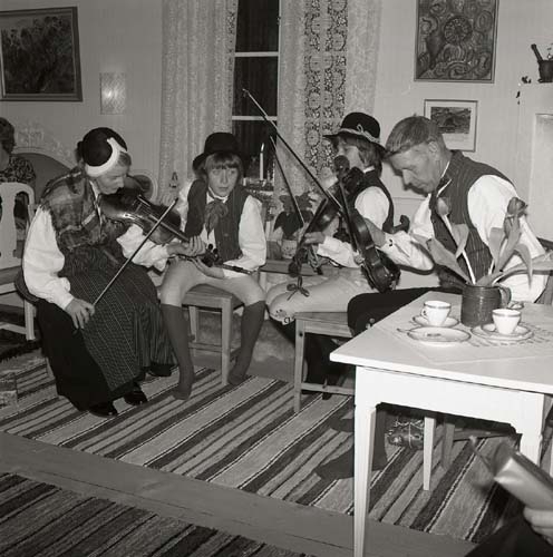 Fyra personer musicerar med sina fioler i ett rum, 1972. De är klädda i folkdräkter.
