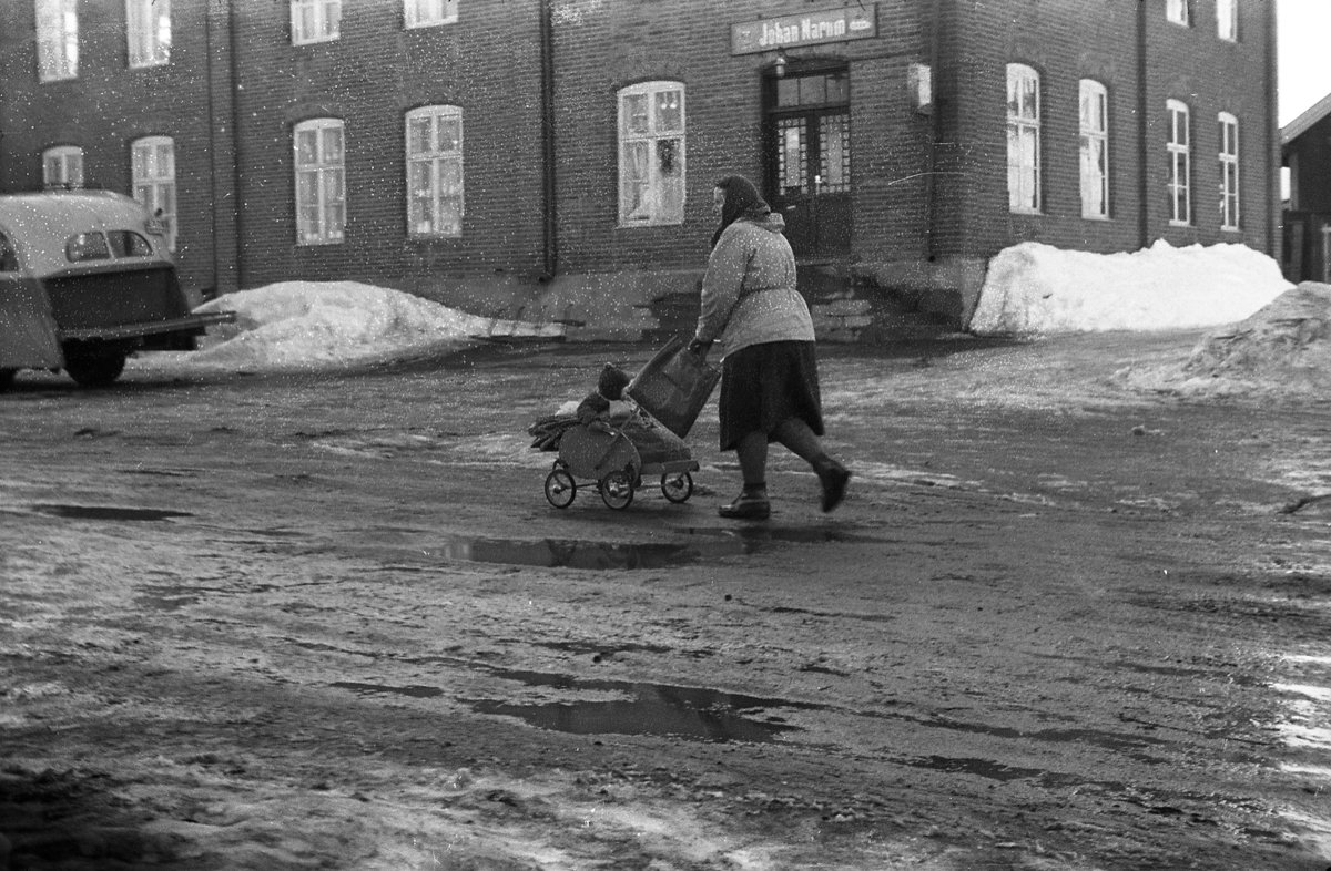 Ei uidentifisert kvinne med barnevogn passerer Narums-butikken på Lena mars 1954.