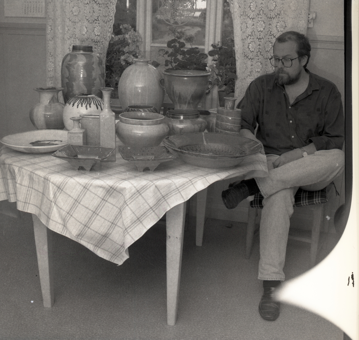 En man sitter vid ett bord fyllt med blomvaser.