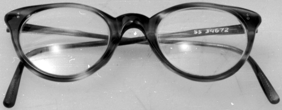 Briller med runde brilleglass og plastinnfatning. Plasten er i ferd med å smuldre opp.