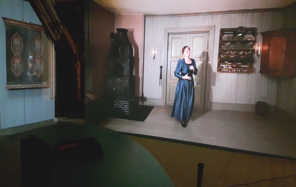 Bilde fra utstillingen BAR1567 hvor man ser en videoprojeksjon av Madam Guldberg som ønsker besøkende velkommen.
