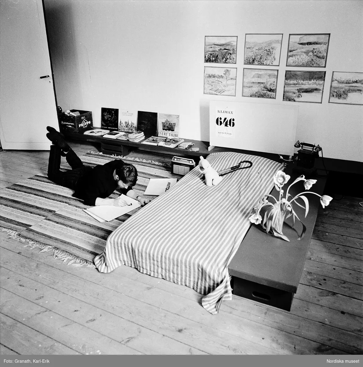 Sovrumsinteriör. Ung man ligger på golvet och läser.