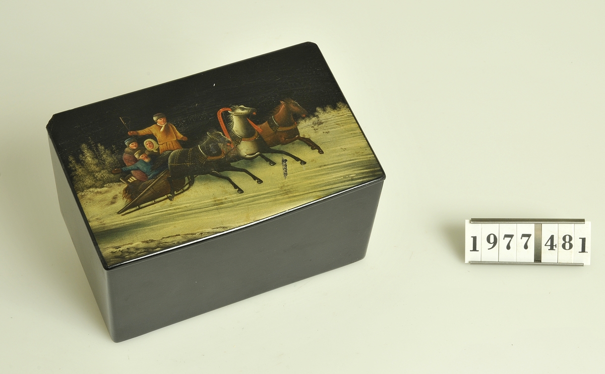 Med lock. Rektangulär form.
Locket fäst på gångjärn av mässing.
Målning på locket: Vinterlandskap med släde
förspänd med tre hästar i bredd.
