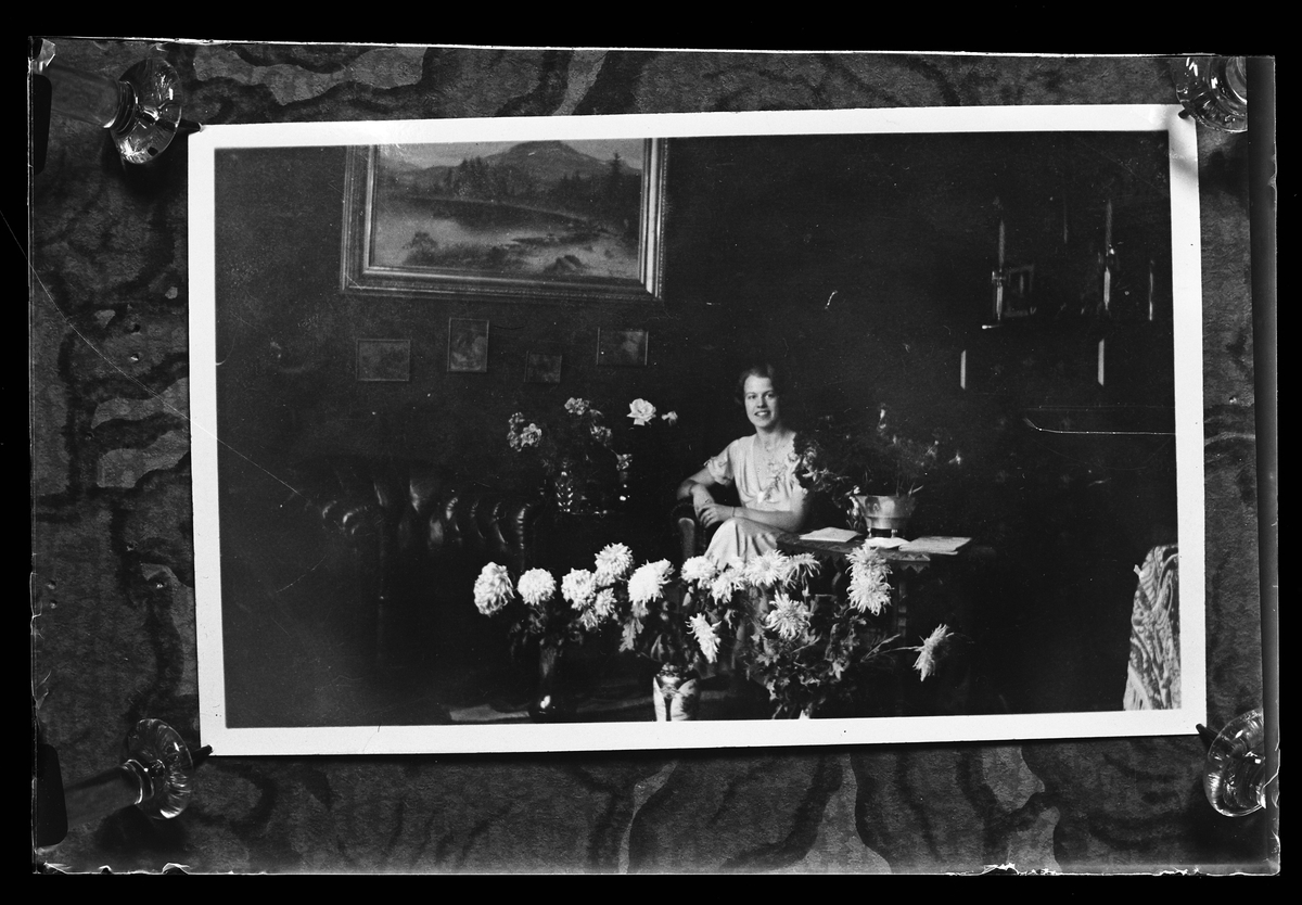 Reprofotografi av ett foto föreställande en kvinna som sitter i ett finrum omgiven av blommor. Troligen i samband med en jämn födelsedag. I fotografens anteckningar står det "Rep. för Ekendahl".
