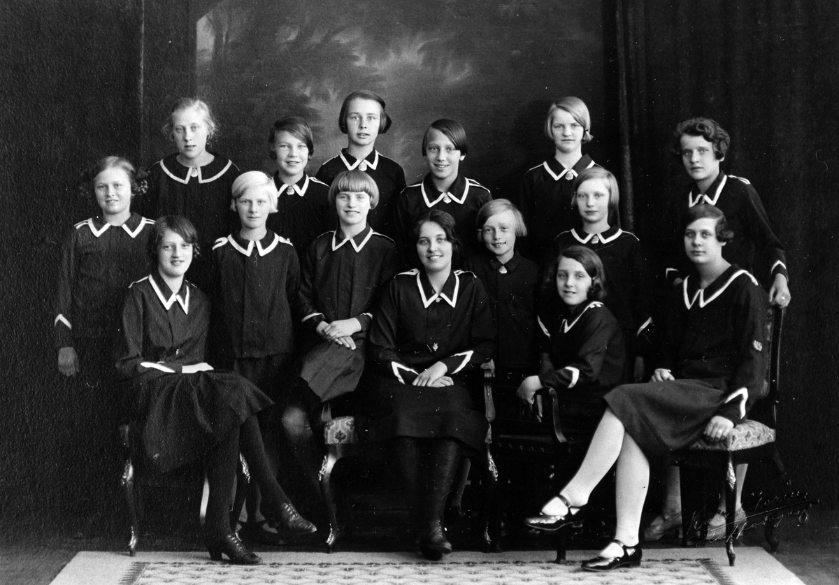 Gruppbild med 13 flickor och 2 kvinnor i uniform, sittande och stående, från Frälsningsarméns Ungdoms- och strängmusikkår.