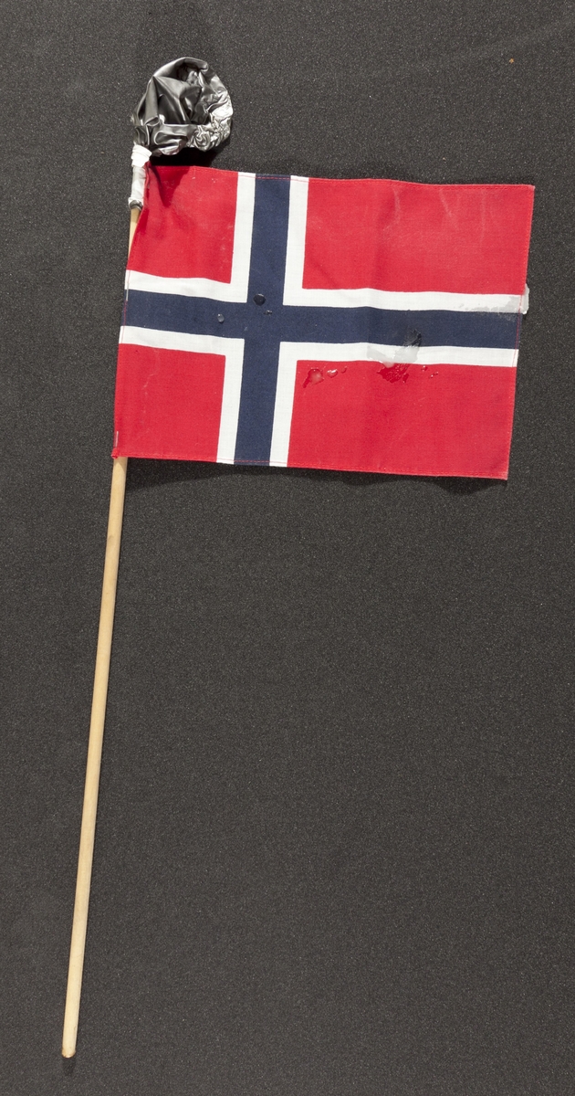 Flagg innsamlet etter terrorhandlingen 22. juli 2011 fra minnesmarkeringene i Lillestrøm. 

Klassisk norsk flagg slik vi kjenner det fra 17.mai feiringer: Blått kors i midten, hvitt kors som "omkranser" det blå (litt tynnere fargefelt) på en rød bakgrunn, de blå og hvite korset går helt til kanten av flagget. Dimensjonene på feltene er slik at de to røde felten mot pinnen er halvparten så store som de to ytterste røde feltene. Flagget brukes både av barn og voksne. På toppen av flaggpinnen er det festet en stålgrå ballong. Den er festet med hvit tape. Ballongen har mistet all luft og ser ut som den har vært i kontakt med varme/ild, da den delevis er tørket og sprø. Det er også sølt stearin flere steder på flagget.