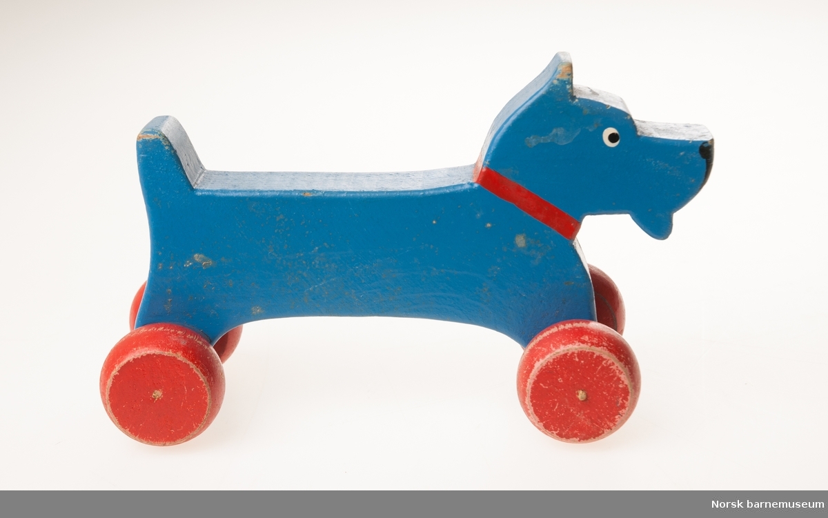 Blå lekehund i tre, på røde bevegelige trehjul.