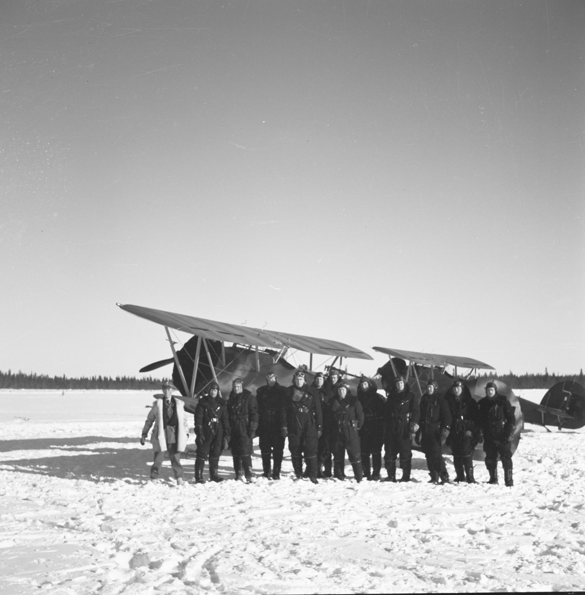 Gruppfoto av flygare från F 19 i Märkäjärvi vid Svenska frivilligkåren i Finland, F 19. I bakgrunden står två flygplan.