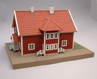 Modell i skala 1:50  av personalbostad, falurött med sadeltak i tegel med vita fönster och skorstenar.
Förstukvisten är valmad med två ingångar via trappor. Innehåller två lägenheter 
om 4 rum och kök. Grönbrun gårdsplan.