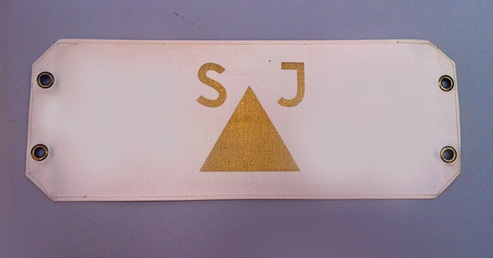 6 armbindlar med rektangulär form i plastad duk. På armbindlarnas vardera kortsidor sitter öljetter för fastsättning med snören.

Följande armbindlar finns:
Jvm 21656:1 Triangel samt bokstäverna SJ i guld på lila botten.
Jvm 21656:2 Triangel samt bokstäverna SJ i guld på vit botten.
Jvm 21656:3 Triangel samt bokstäverna SJ i guld på röd botten.
Jvm 21656:4 Triangel samt bokstäverna SJ i guld på gul botten.
Jvm 21656:5 Triangel samt bokstäverna SJ och två rektanglar i guld på silvergrå botten.
Jvm 21656:6 Triangel samt bokstäverna SJ i guld på orange botten.