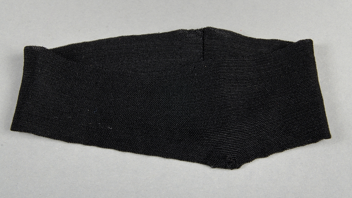 Sorgband i svart elastiskt material (konstsilketrikå?).
