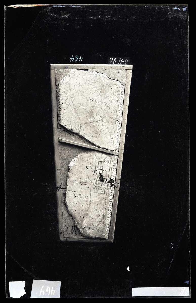 Middelaldersk gravstein, to fragmenter (muligens fra to ulike steiner) fra Nidarosdomen. Tekst rundt kanten og figurer på overflaten.