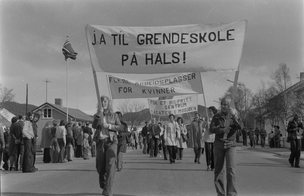 1.Mai-tog i Mosjøen 1975, demonstrasjonstog i Elvegata. 
Paroler: "Ja til grendeskole på Hals" Huset til venstre er revet.