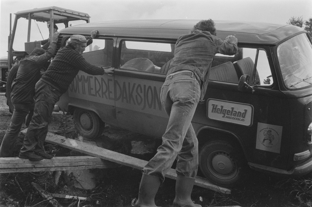 Helgeland Arbeiderblads sommerredaksjon har kjørt i grøfta på sør-offersøy ved butikken.
Arbeid med å få bilen opp av grøfta. Menn som dytter og traktor.