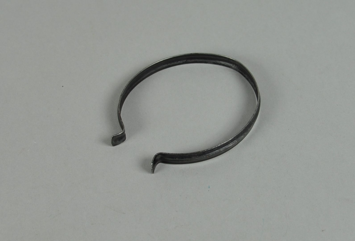 Bukseklemme av metall. Oval form med åpning i den ene enden, og utstående endestykker.
