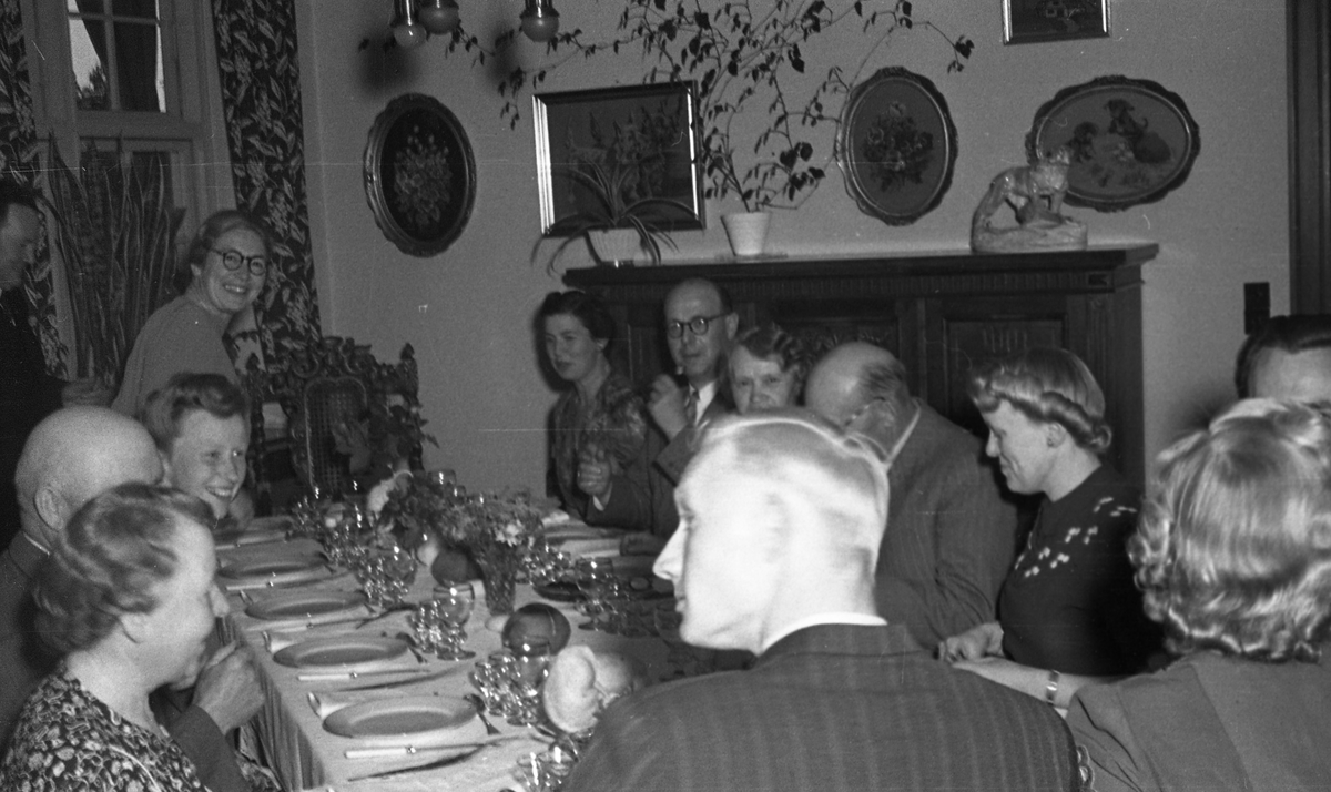 Middag. Gruppebilde med tretten personer. Seks menn og syv kvinner samlet rundt middagsbordet. Suderøy på vei til fangstfeltet.