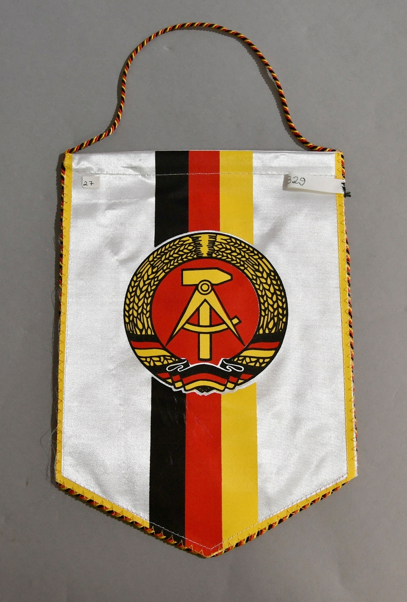 Hvitt bordflagg med spiss nederst og tvinnet snor i rødt, gult og svart rundt vimpelen. Striper i svart, rødt og gult, med riksvåpenet for Øst-Tyskland på midten.