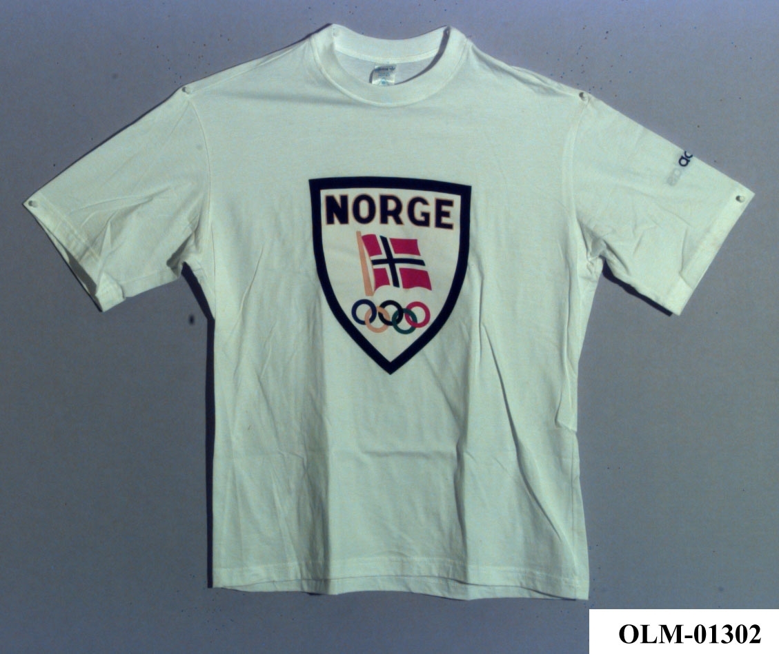 T-skjorte med våpenskjold på brystet, med tekst NORGE, norsk flagg og olympiske ringer