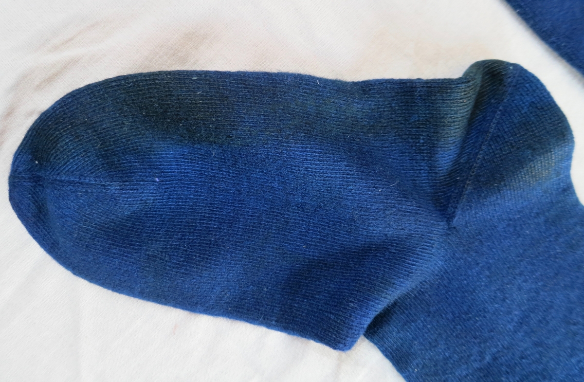blå sockor/strumpor av ullgarn. hemstickade med brudgumskrus upptill, dvs. ca 30 varv mönster. Nådde till ovanför knäna "så långt benen räckte". Färgade i "byttblått".