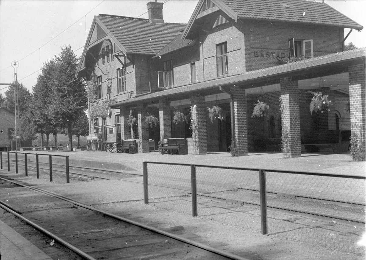Båstad Södra järnvägsstation, ursprungligen uppförd 1885 av Skåne Hallands Järnväg, SHJ. SHJ förstatligades 1896 och stationen tillbyggdes av SJ med bl a övervåning vid sekelskiftet. Loggian, pelargången, till höger tillkom 1935, då också expedition, biljetthall och resgodsmagasin byggdes ut.