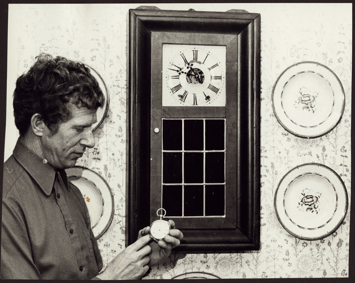 Sven Ågren visar upp en raritet från sin klocksamling, en amerikansk Waltham i vitt guld. På väggen hänger ett farmarur.
Foto Ragnar Eriksson