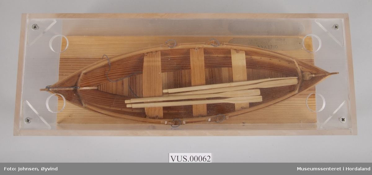 Båtmodell av Oselvar med to par årer. Satt i monter av pleksiglass og tre.