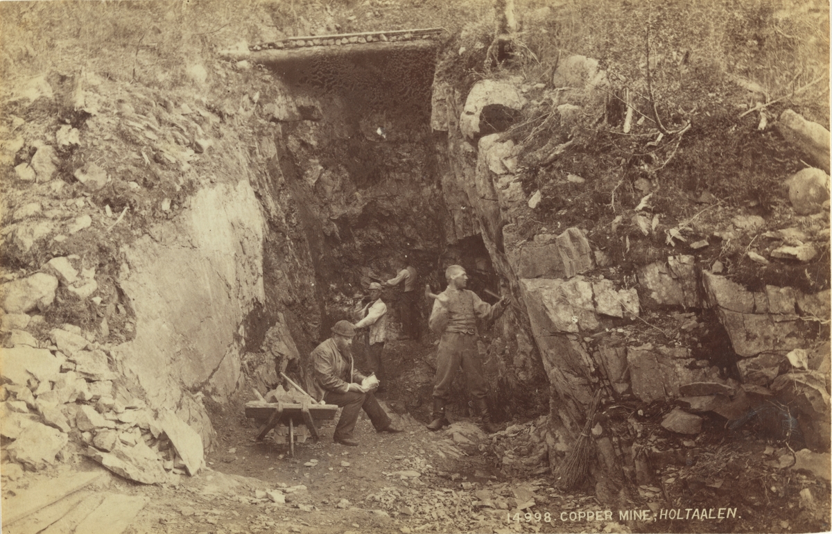 Fra kobbermine i Holtålen, Sør-Trøndelag. Tre menn jobber med hammer og meisel, én sitter og undersøker en stein. Fotografert mellom 1870 og 1886.