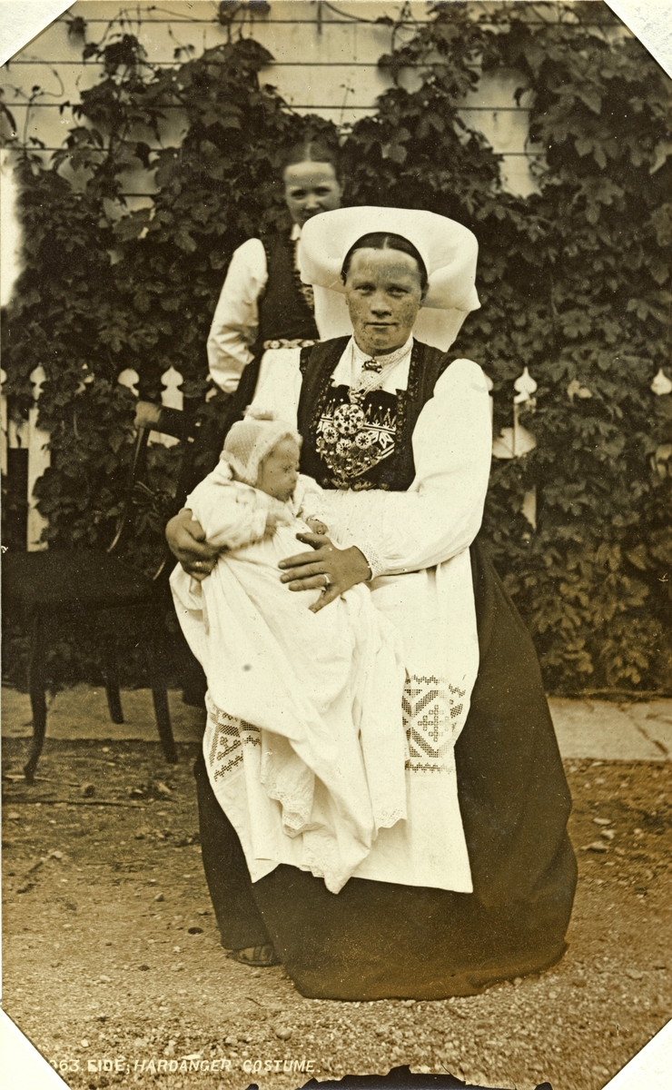 Kvinne i Hardangerdrakt med dåpsbarn på fanget. Fotografert mellom 1870 og 1886.