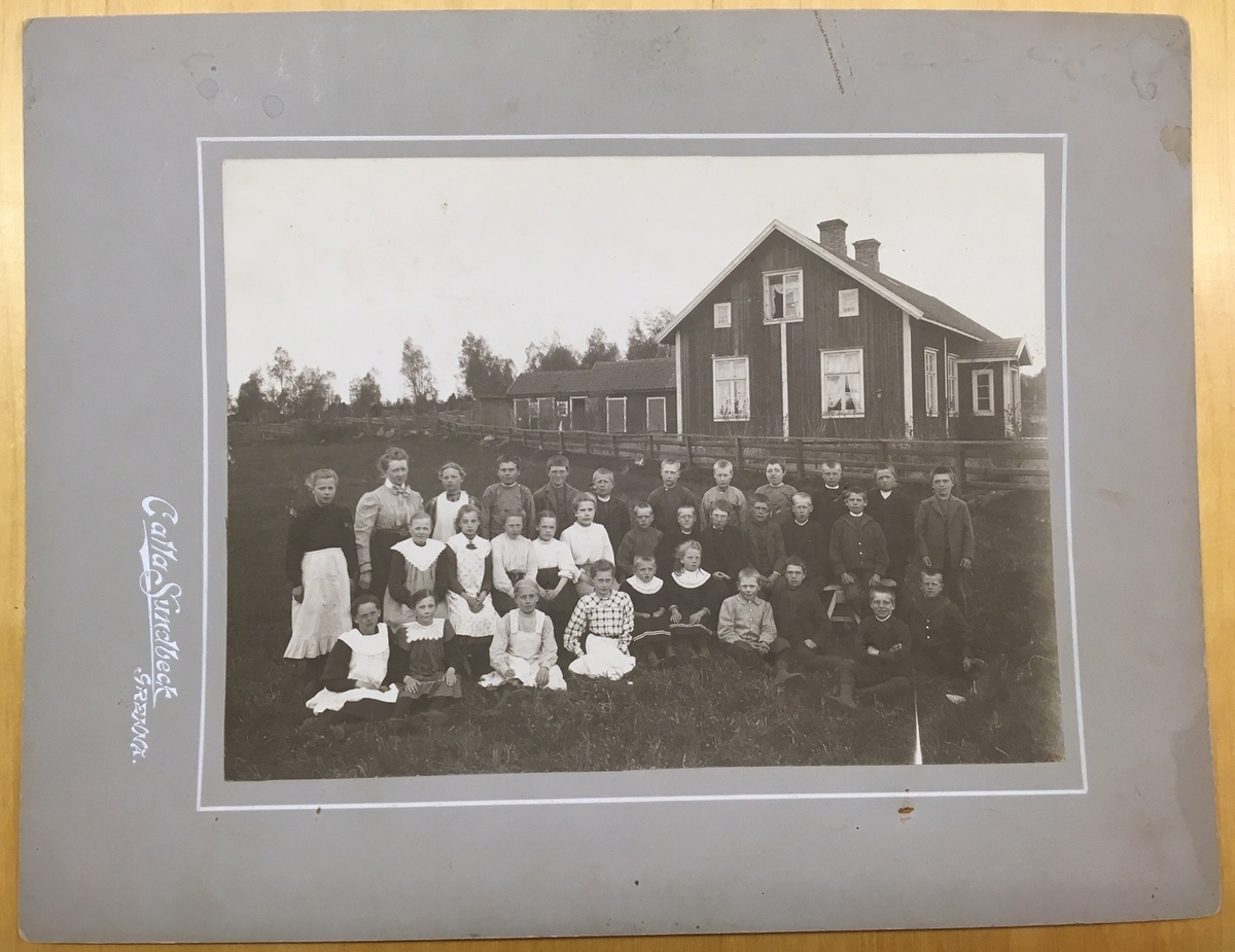 Folkskolelärarinnan Charlotta Kristina Johansson med skolbarn, sittande och stående på en äng vid sidan av Mörstorps skola.