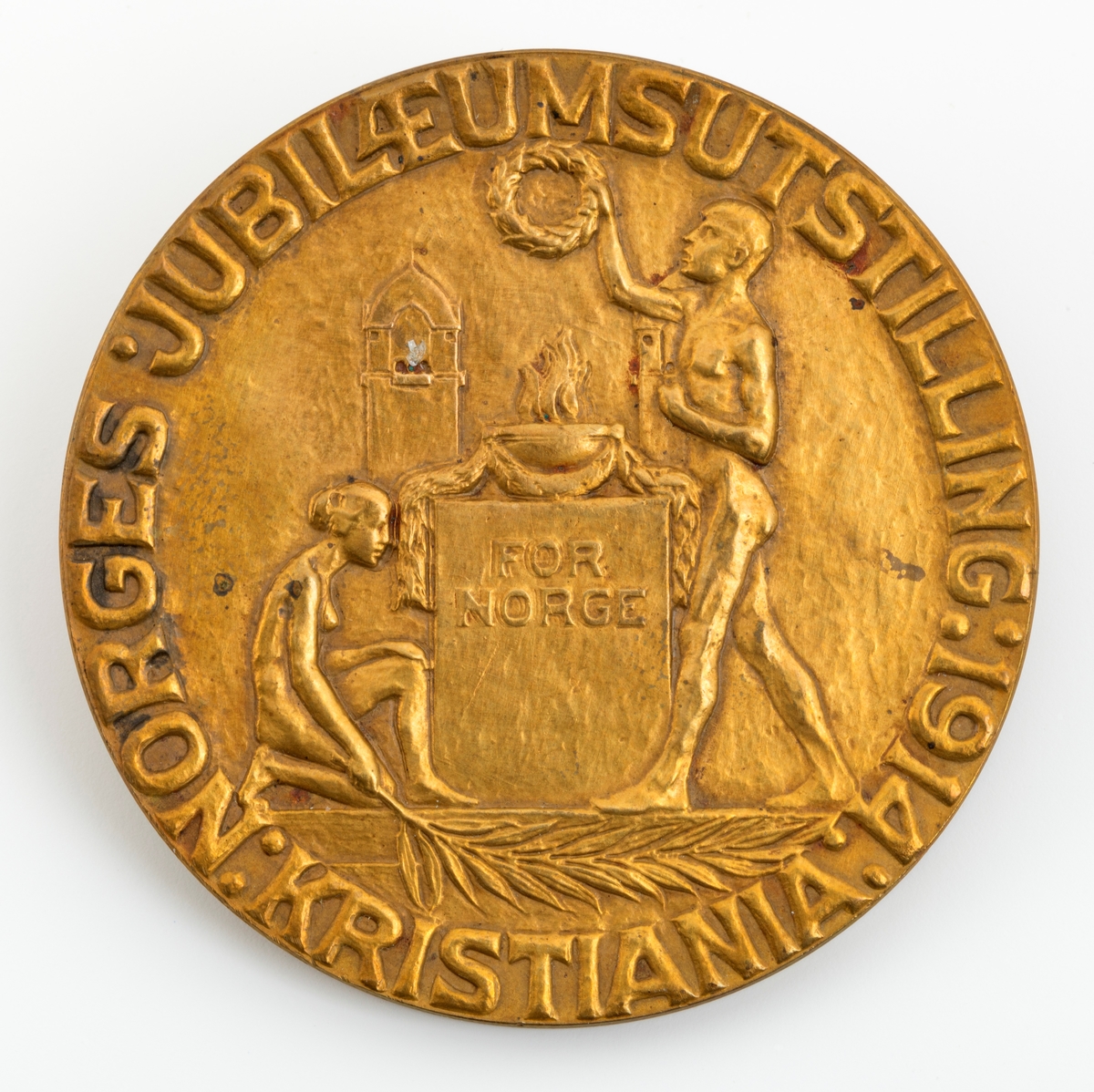 Denne sølvmedaljen fikk Ole Jacobsen Vestby (1875-1954) i 1914 på jubilæumsutstillingen som ble avviklet på Frogner i Oslo (da Kristiania), for å markere at det var 100 år siden Norge fikk sin egen grunnlov og dermed en betydelig selvstendighet, til tross for personalunionen med den svenske kongen som statsoverhode (fram til 1905). Medaljen er sirkelrund og overflater som er prydet med et relieffer. På den ene sida er det et motiv med to nakne mennesker, ei kvinne og en mann. Kvinna sitter på huk ved en sokkel som danner underlag for et kar som det kan se ut til å komme ildtungfer opp av. Kvinna holder et diger blad i den ene handa. Mannen står på den andre sida av sokkelen og holder en krans over over sokkelen. På den andre sida er riksvåpenet - et skjold med en stilisert stående løvefigur som holder ei øks i forlabbene - det sentrale motivet. Omkring dette heraldiske symbolet er flata utfylt med greiner av bartre med kongler. Øverst på denne bildeflata er årstallene 1814 og 1914 plassert. Nederst, under riksvåpenet er det et horisontalt bånd der mottakerens navn - OLE J. VESTBY - er inngravert. 

Jubileumsutstillingen skulle være en manifestasjon av kvaliteter som preget nasjonen Norge, og særlig næringslivsaktørene som var inviterte til å presentere seg, sine produkter og den samfunnsnytten de gjorde. Som mange utstillinger  Dette er åpenbart en medalje som ble produsert i mange eksemplarer for pågravering av navnene til de som juryene fant verdige til å bli hedret. Ole Jacobsen hadde åpenbart spesielle håndverksferdigheter, og han arbeidet i et formspråk som fortsatt var trendy i 1914. I ettertid har flere antydet at årsaken til at Vestby ikke fikk gullmedalje, var at han ikke hadde smidd knivbladene sjøl. Det var det en smed i Romedal som hadde gjort. Bladene hadde en god håndverksmessig standard, men hadde ikke de spesielle kunstneriske kvalitetene som preget Vestbys slirer og skaft.