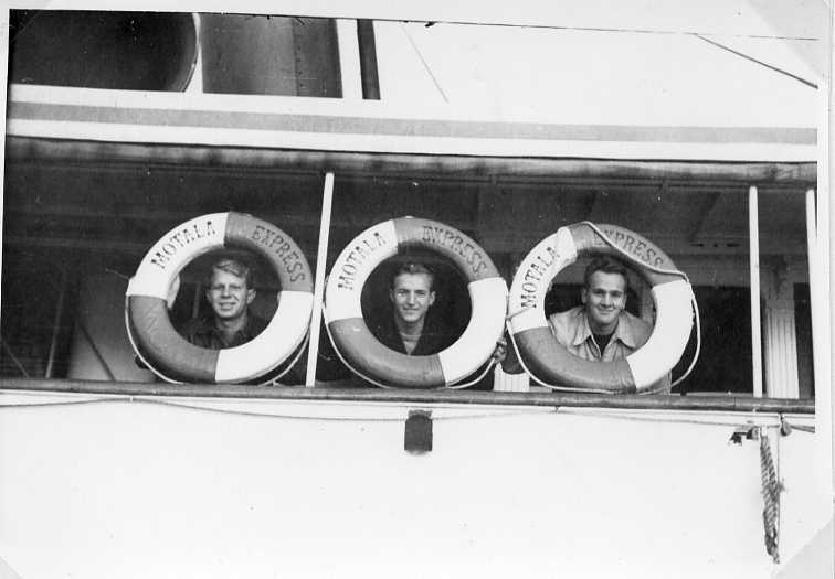 Tre unga män kikar ut genom livbojar märkta Motala Express. De befinner sig på samma fartyg. Till vänster sannolikt L T Sanford