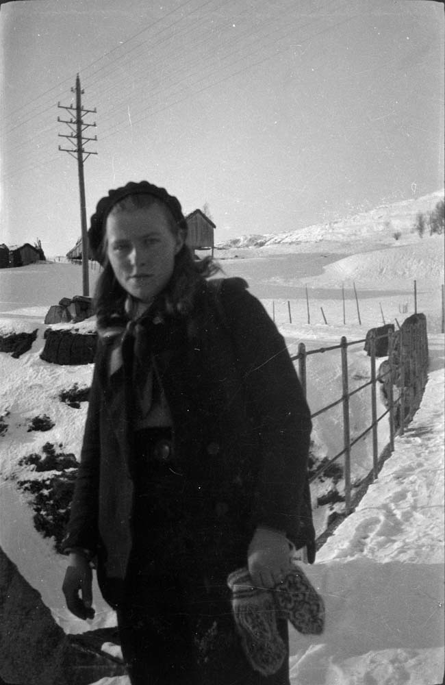 Kvinne med votter i en hånd, står på bro i snøen.