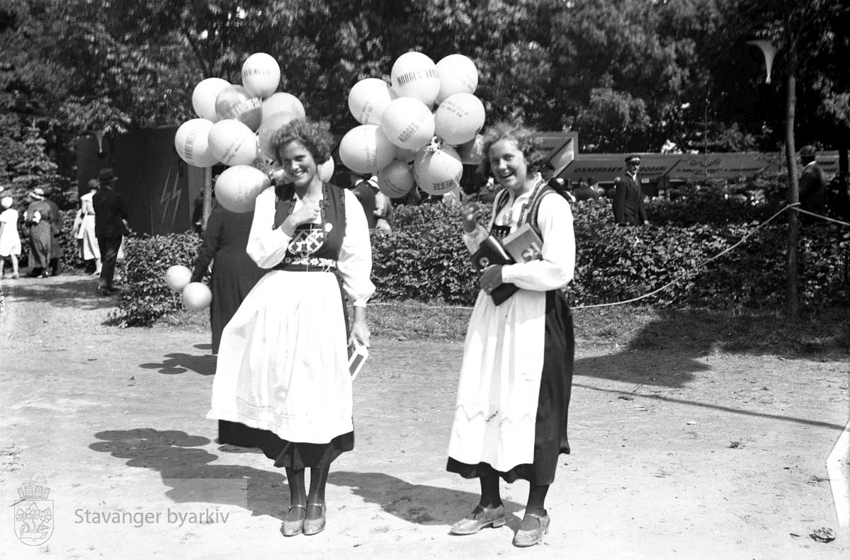 Varemessens filmer..To kvinner i bunad, med reklameballonger .Norges varemesse