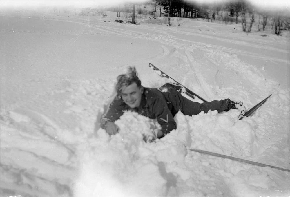 Soldat ligger i snøen med et stort smil etter å ha falt på ski.