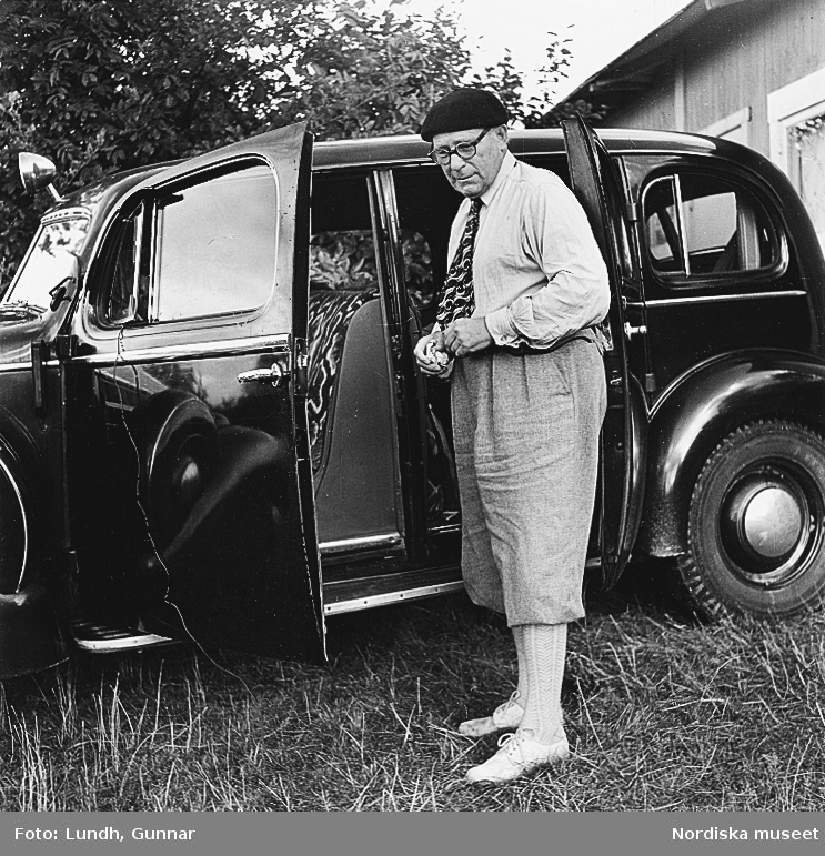 En man i basker och golfbyxor (äppelknyckarbyxor) står vid en Cadillac årsmodell 1936. bilden tagen i Skåne år 1950.