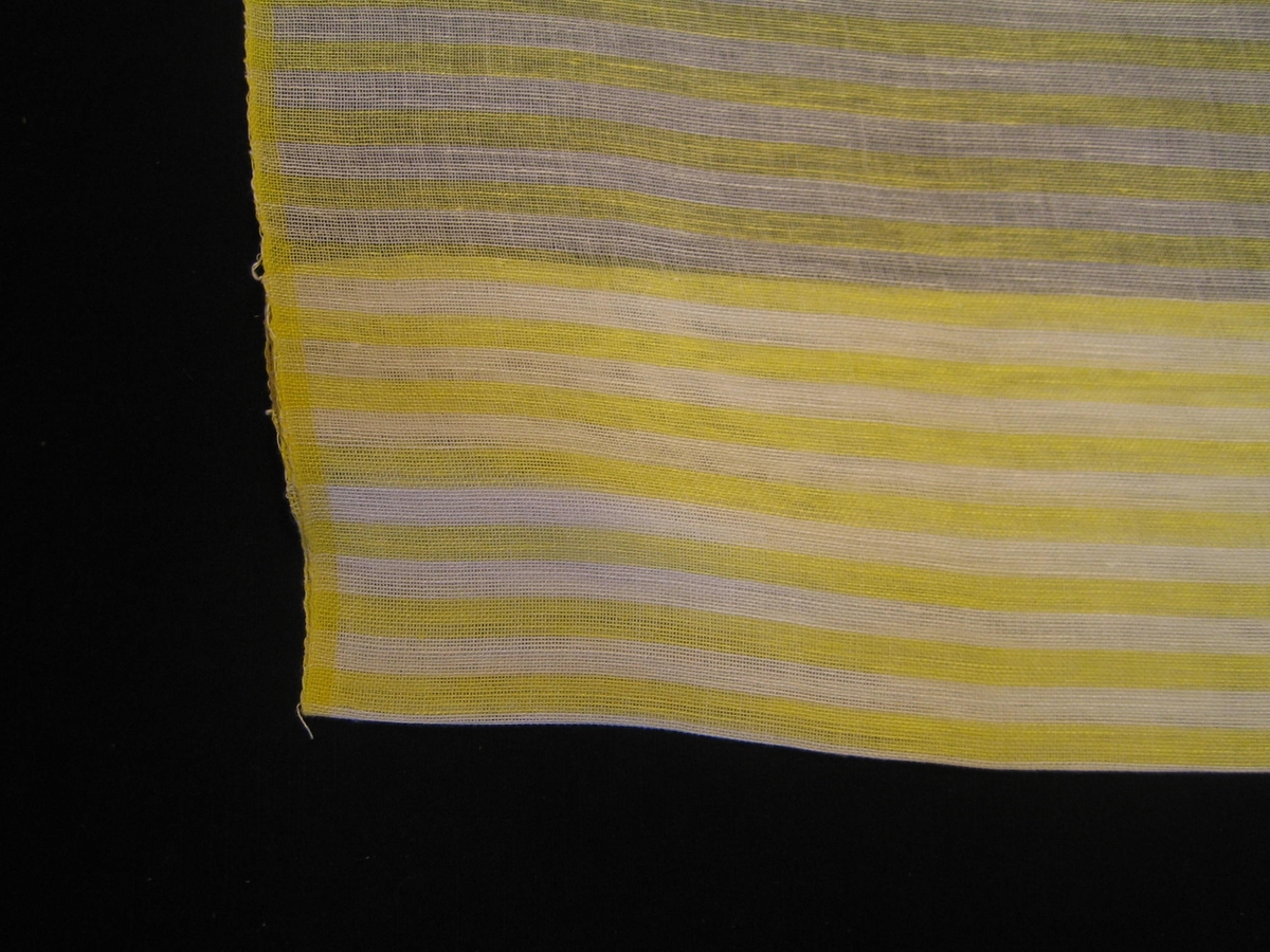 Gardin i vitt och gult randig på tvären, väv i tuskaft med 8 mm breda ränder i vitt och gult. Gardinen är vävd i bomull i varp och lin i inslag. Stadkanterna är varpade i gult 10 mm. Komponerad Ann-Mari Nilsson.